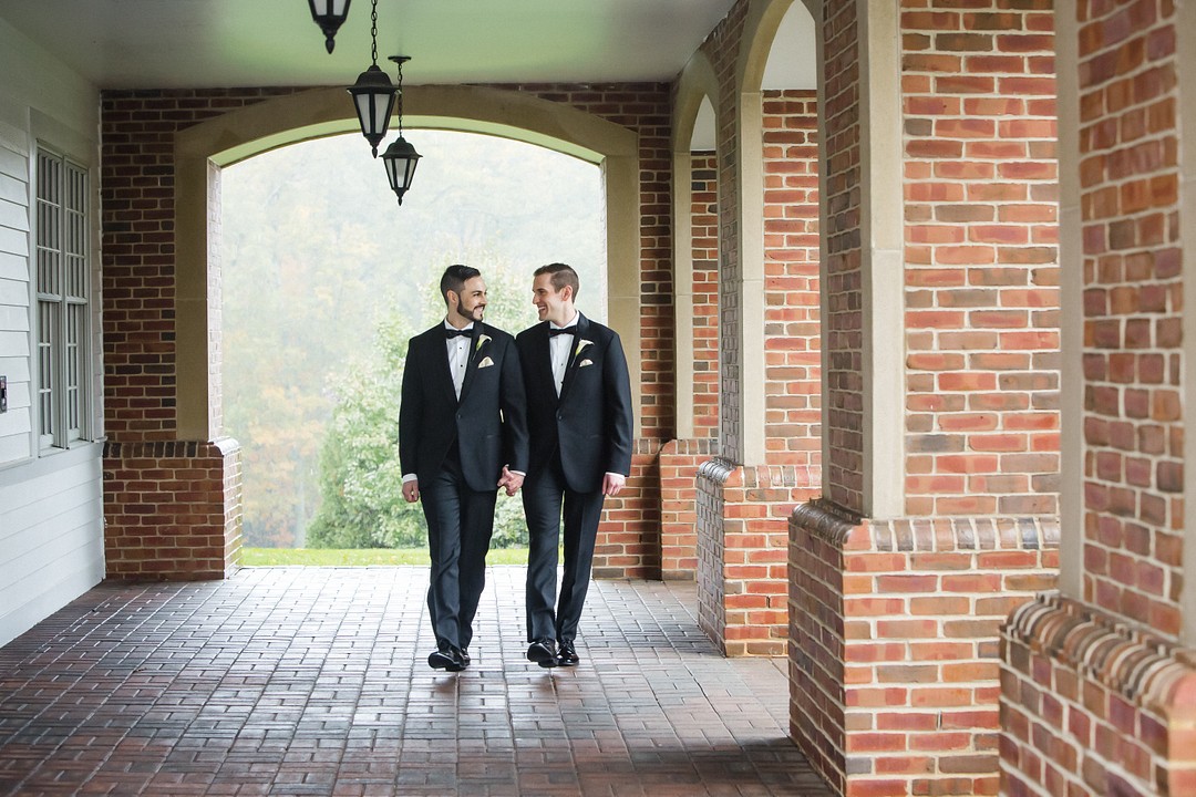 two groms holding hands walking through wedding venue