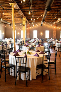 barn with wedding reception tables, purple napkins, white linen