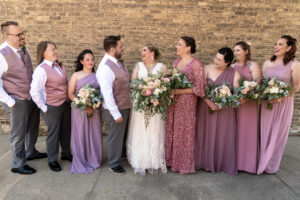bride standing with wedding party in rose, mauve and periwinkle dresses and suits