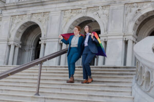 lesbian couple standing on steps of library of congress holding rainbow flag around them