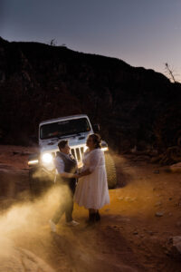 lesbian couple standing in front of car in the desert at their wedding